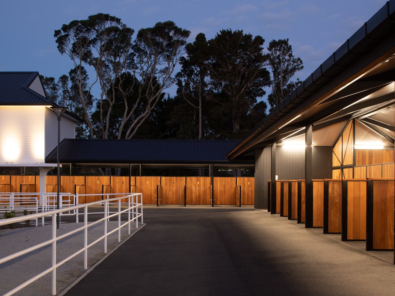 Evening view of Auckland Racing Club stables complex with illuminated horse stalls and white fencing under a clear sky