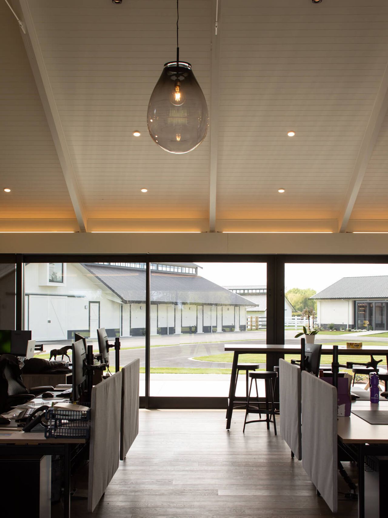 Office space at Cambridge Stud Farm with expansive glass windows overlooking equine-focused architecture, including stables and landscaped pathways, blending modern workplace design with the farm's equestrian heritage in New Zealand.