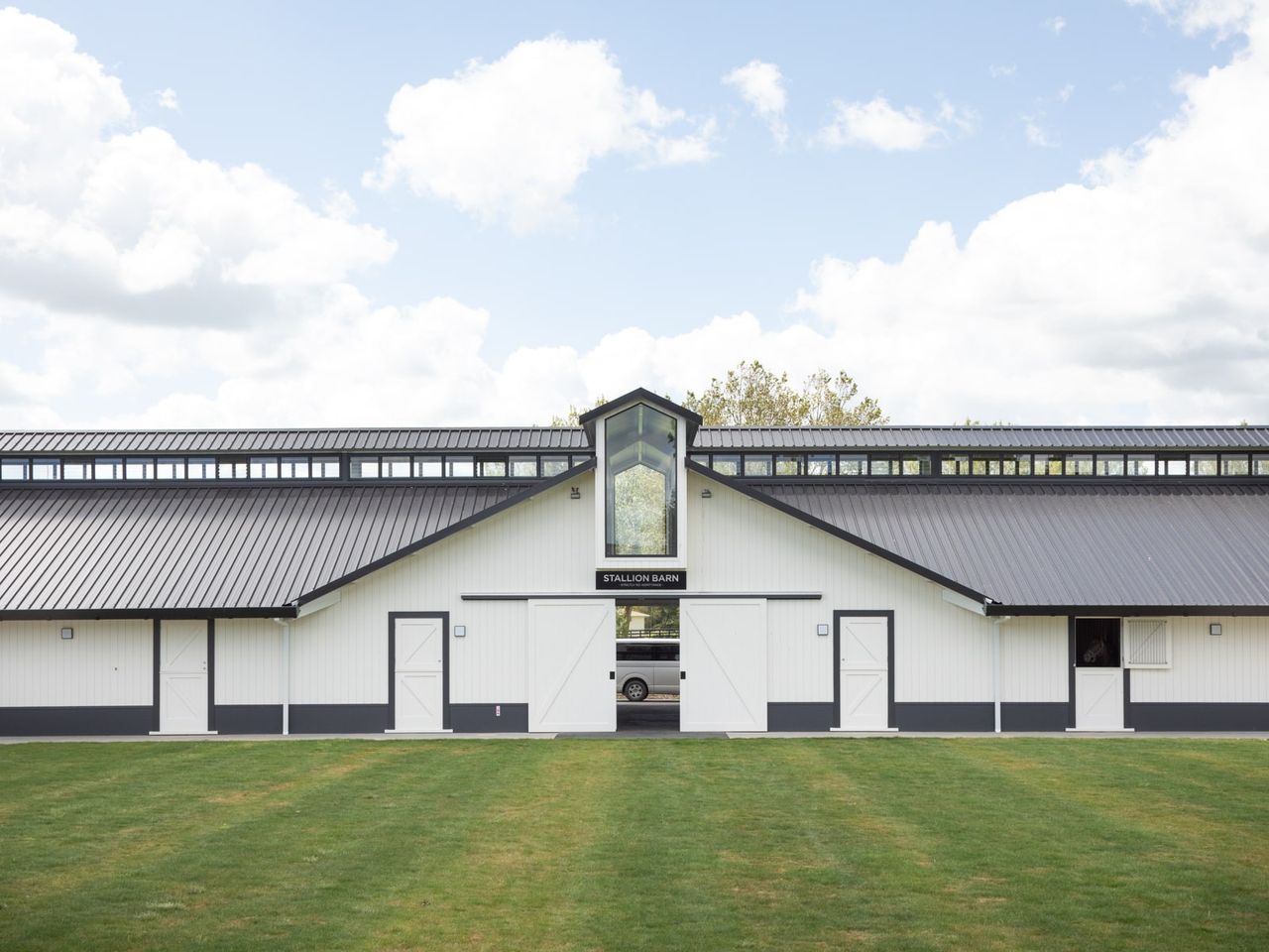 Front view of the Stallion Barn at Cambridge Stud Farm, showcasing modern equine architecture with a sleek black roof, white paneling, and ample natural lighting. This purpose-built structure highlights functionality and aesthetic appeal, designed specifically for equine care and breeding.