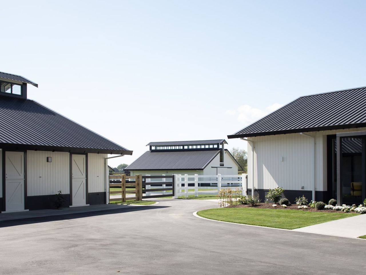 Close-up view of the stables at Cambridge Stud Farm, featuring sleek black roofs, white facades, and manicured landscaping. The layout showcases modern equine architecture designed for efficiency and aesthetics, set within a tranquil rural environment.
