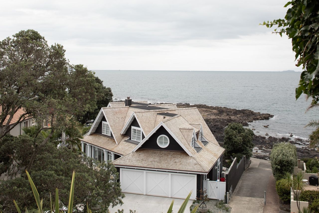 Oceanfront Cape Cod home in Milford with cedar shingles, white trim, and a private driveway leading to rocky shoreline.