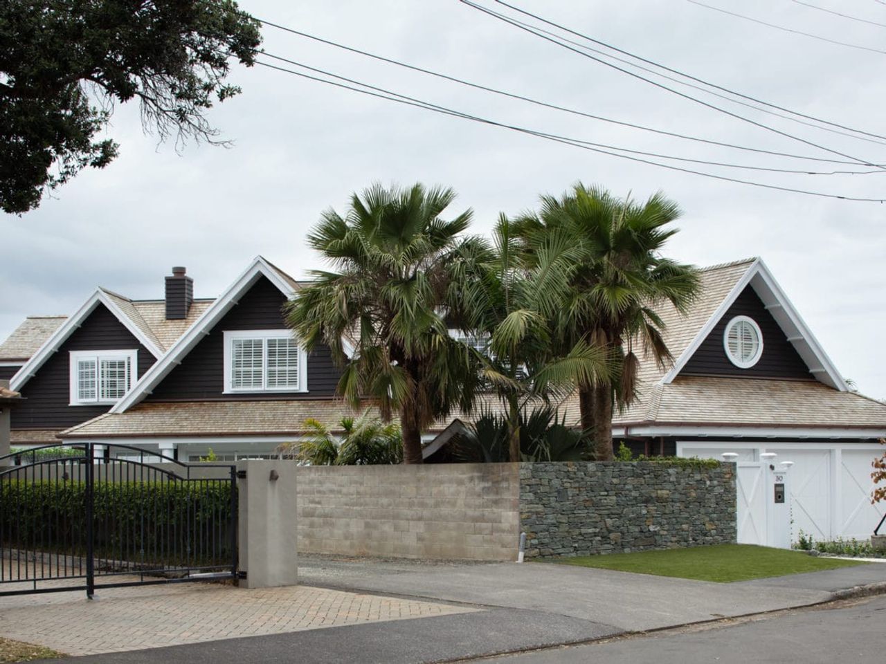 Front view of a Cape Cod home in Milford, framed by palm trees, stone walls, and a gated driveway.