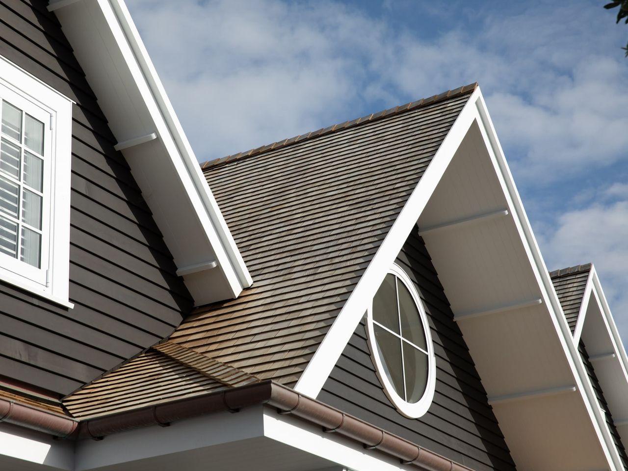 Close-up of the gabled roof and round window of an award-winning Cape Cod home in Milford, featuring classic wood siding and white trim.