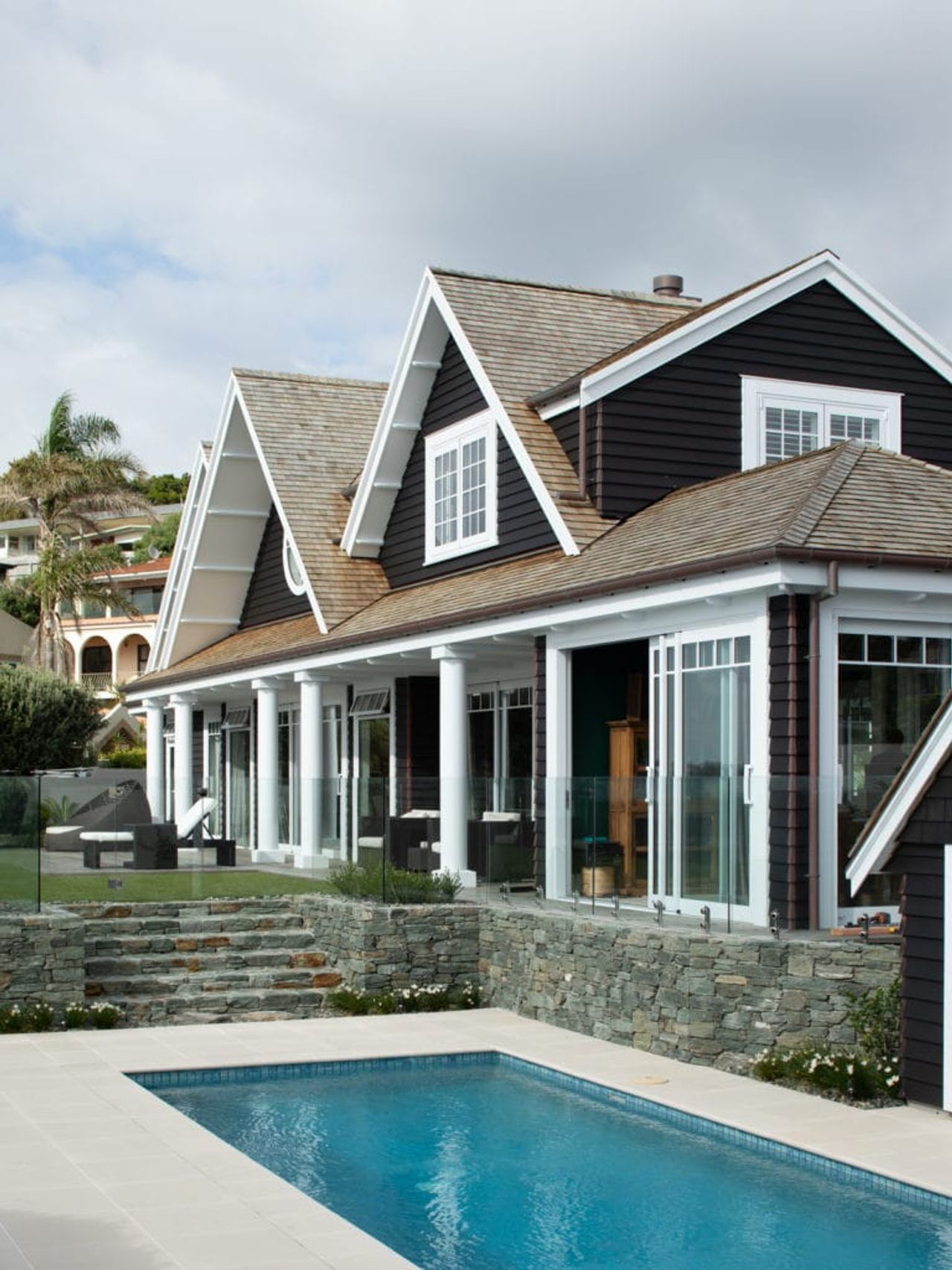 Backyard of an award-winning Cape Cod home in Milford, featuring a pool, stone patio, and classic gabled architecture.