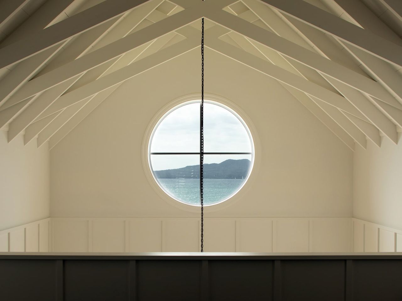 Interior of a Cape Cod home in Milford, featuring a vaulted ceiling with exposed beams and a round window overlooking the ocean.