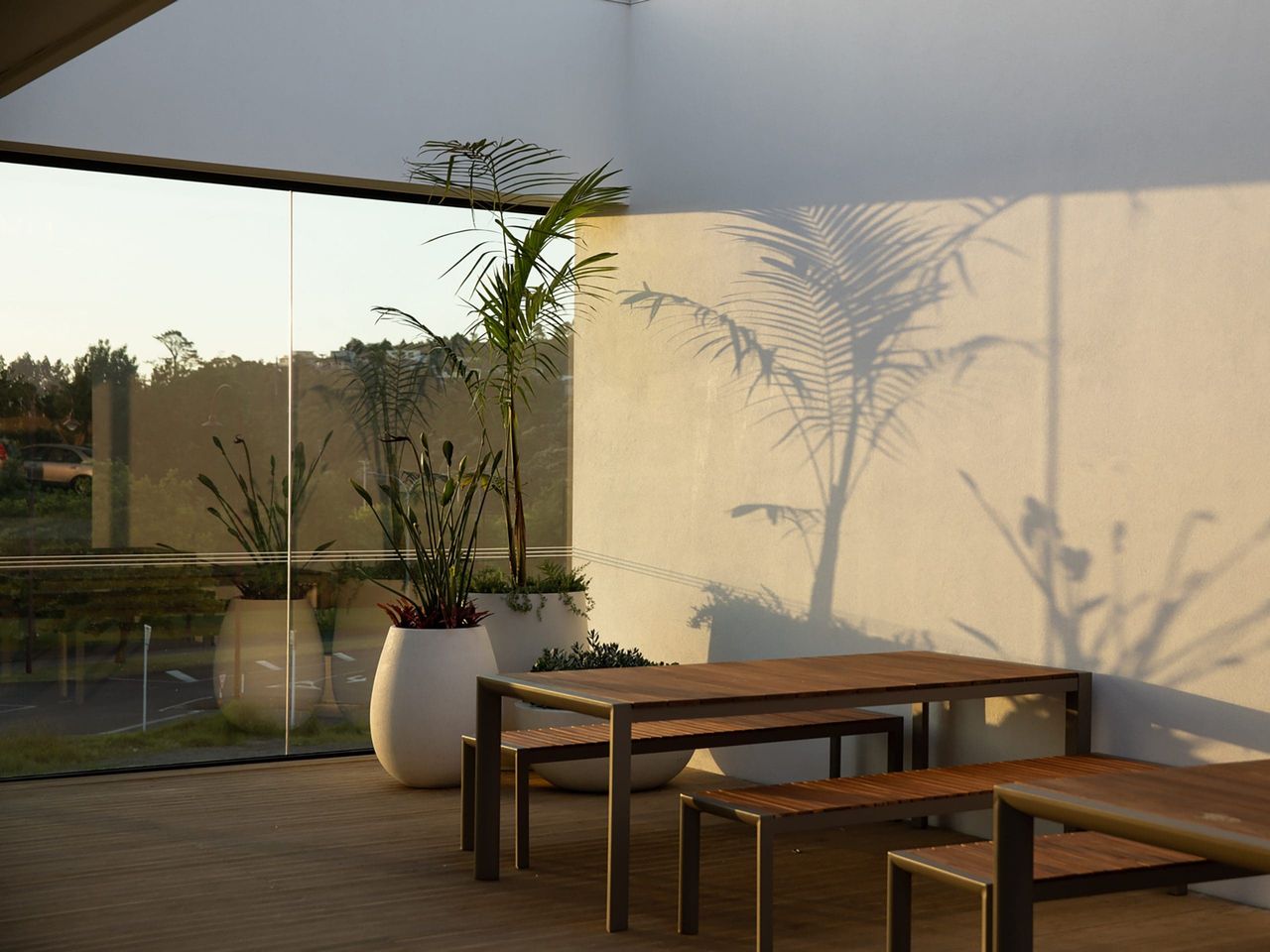 Outdoor seating area at Fields Cafe by OKLA, featuring modern wooden furniture, potted plants, and soft natural light, blending contemporary design with a relaxing atmosphere in New Zealand.