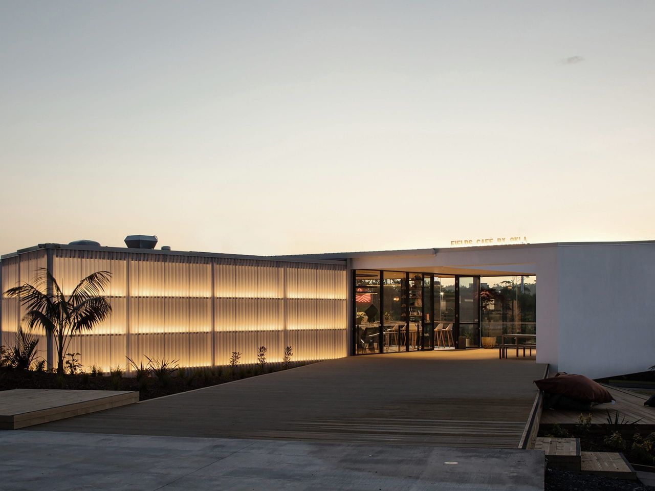 Exterior view of Fields Cafe by OKLA at sunset, showcasing modern hospitality architecture with glowing facade panels and a sleek entrance in New Zealand.