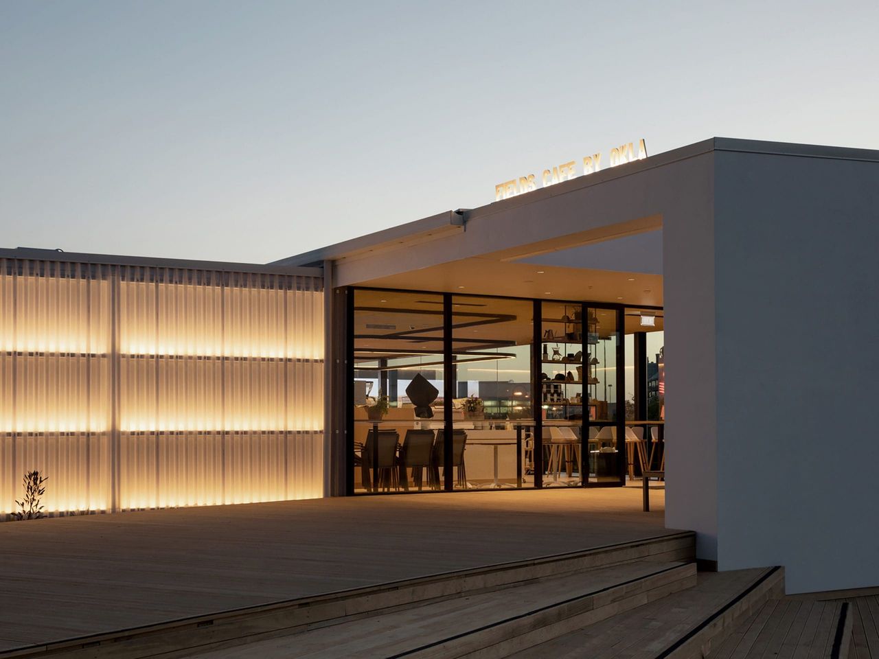 Twilight view of Fields Cafe by OKLA, highlighting illuminated architectural panels, inviting glass doors, and warm interior lighting, showcasing modern hospitality architecture in New Zealand.