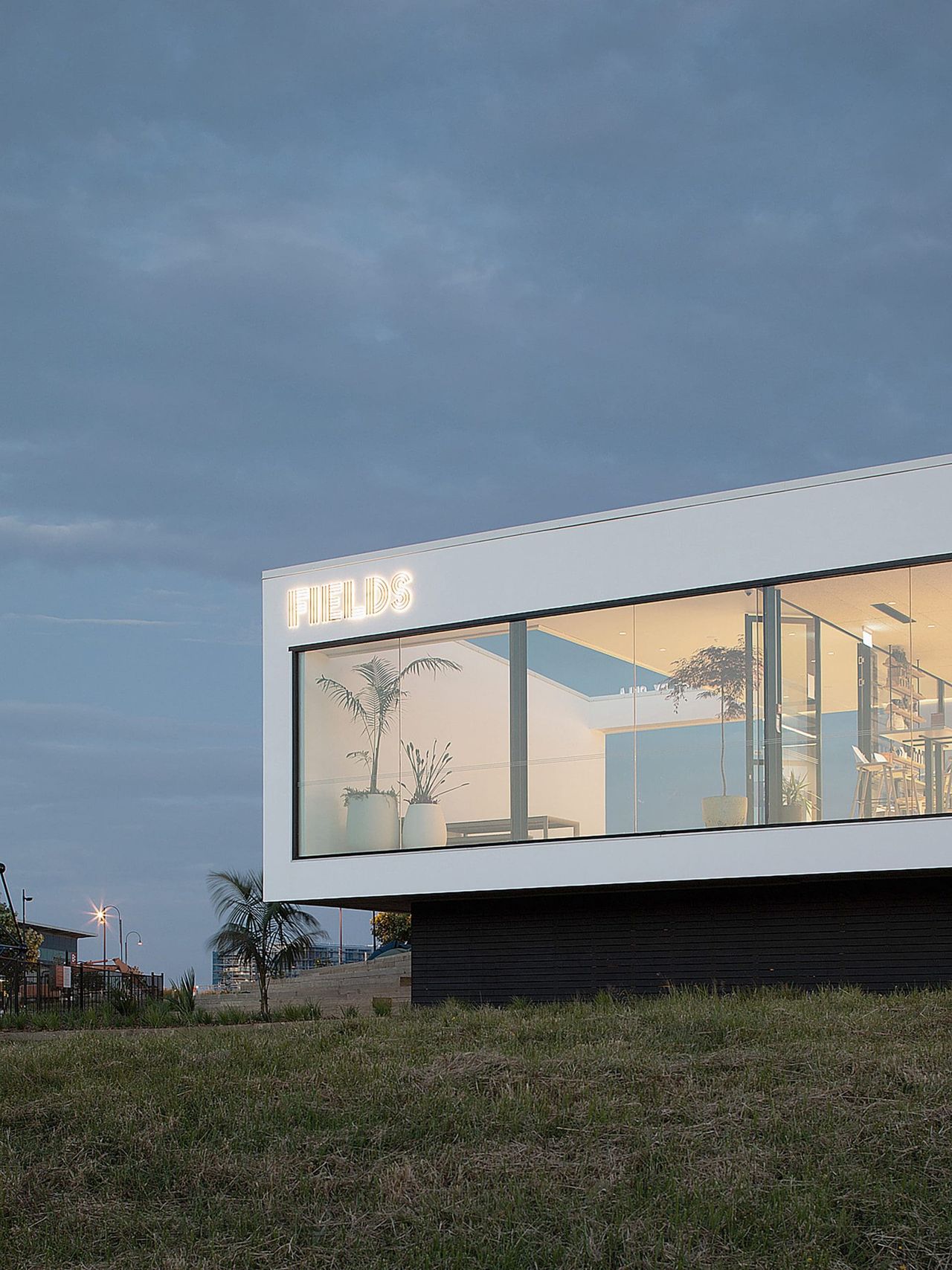 Elevated view of Fields Cafe by OKLA, showcasing its modern architecture with large glass windows, minimalist design, and natural surroundings, blending contemporary style with a New Zealand landscape.
