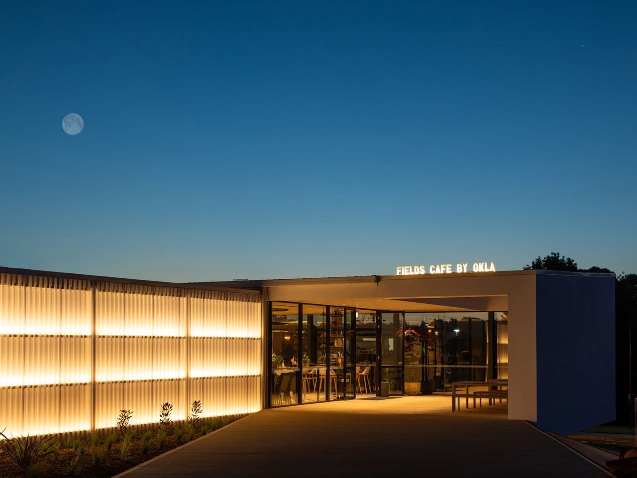Modern architectural design of Fields Cafe by OKLA at dusk, featuring illuminated exterior panels and sleek glass entrance, showcasing contemporary hospitality architecture in New Zealand.