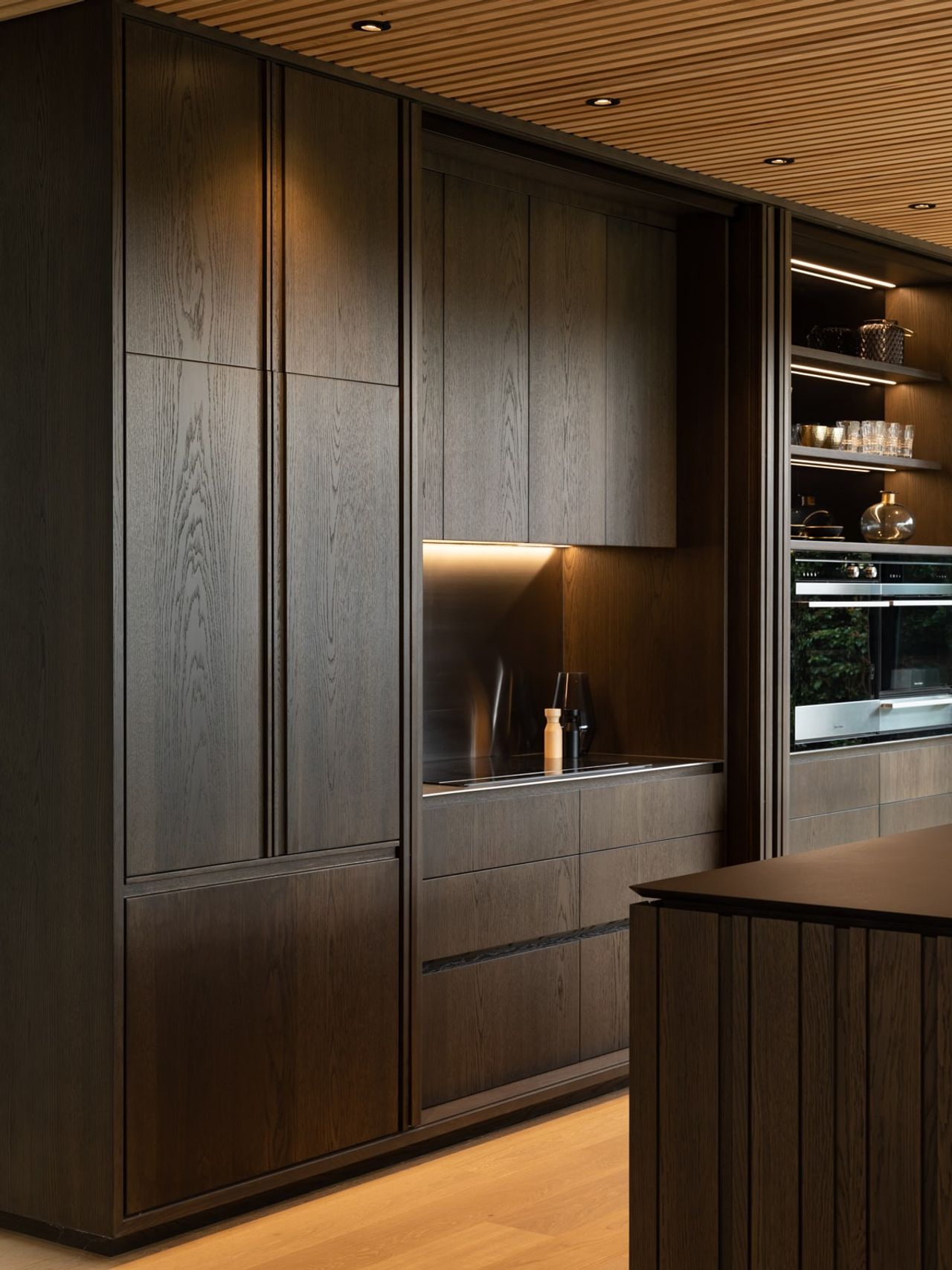 Close-up view of the Karaka Lake Showhome kitchen featuring dark wood cabinetry, integrated appliances, and subtle lighting accents. This sophisticated interior design showcases modern architectural elegance by Young+Richards+ in New Zealand.