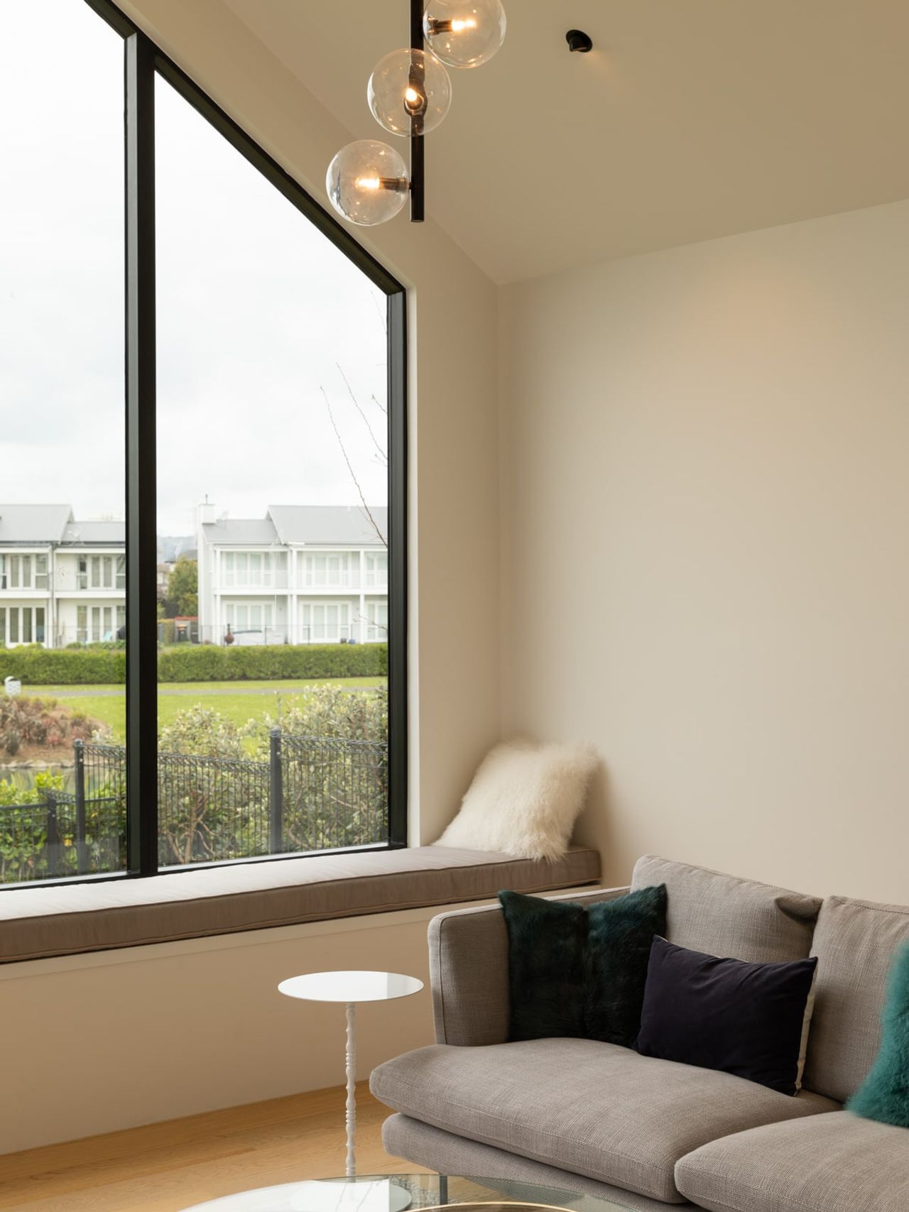 Cozy living space in the Karaka Lake Showhome featuring a large picture window with built-in seating, modern lighting fixtures, and plush furnishings. A beautiful example of contemporary interior design and home architecture by Young+Richards+ in New Zealand.