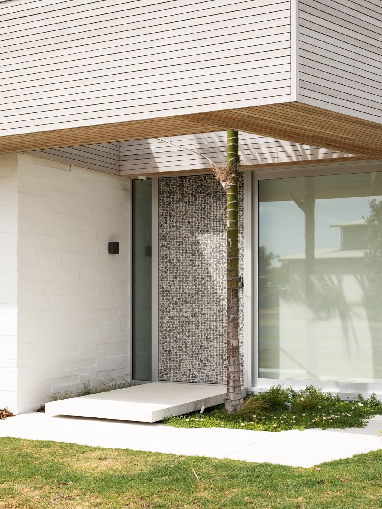 Entrance of the Modern Beach Pad featuring a mosaic-tiled accent wall, floating concrete step, and modern white cladding