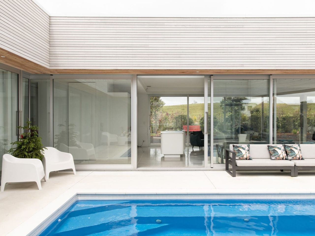 Modern Beach Pad courtyard featuring a sleek pool, white lounge chairs, and large glass sliding doors connecting indoor and outdoor spaces