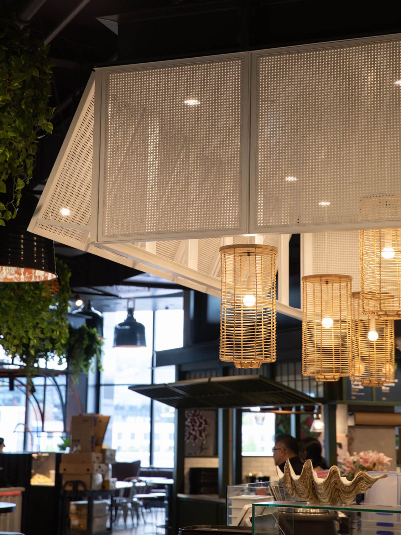 Close-up of modern interior design details at Poke House in Westfield Mall, featuring perforated metal paneling, warm rattan pendant lights, and lush greenery accents. A stylish hospitality space in Auckland.