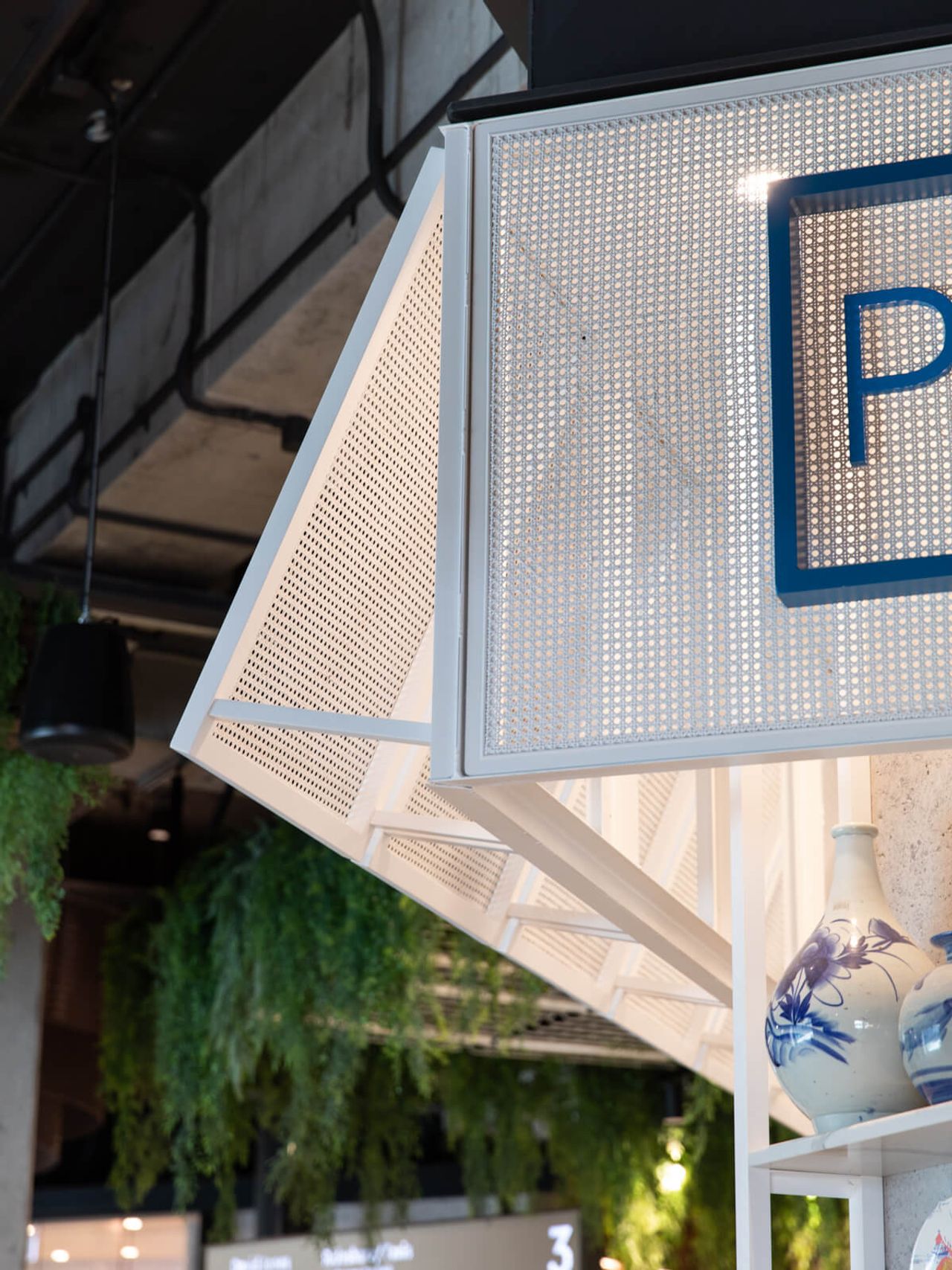 Close-up of Poke House restaurant's modern perforated metal design, complemented by decorative ceramic vases and lush greenery. A sleek and stylish interior detail in Auckland's Westfield Mall.