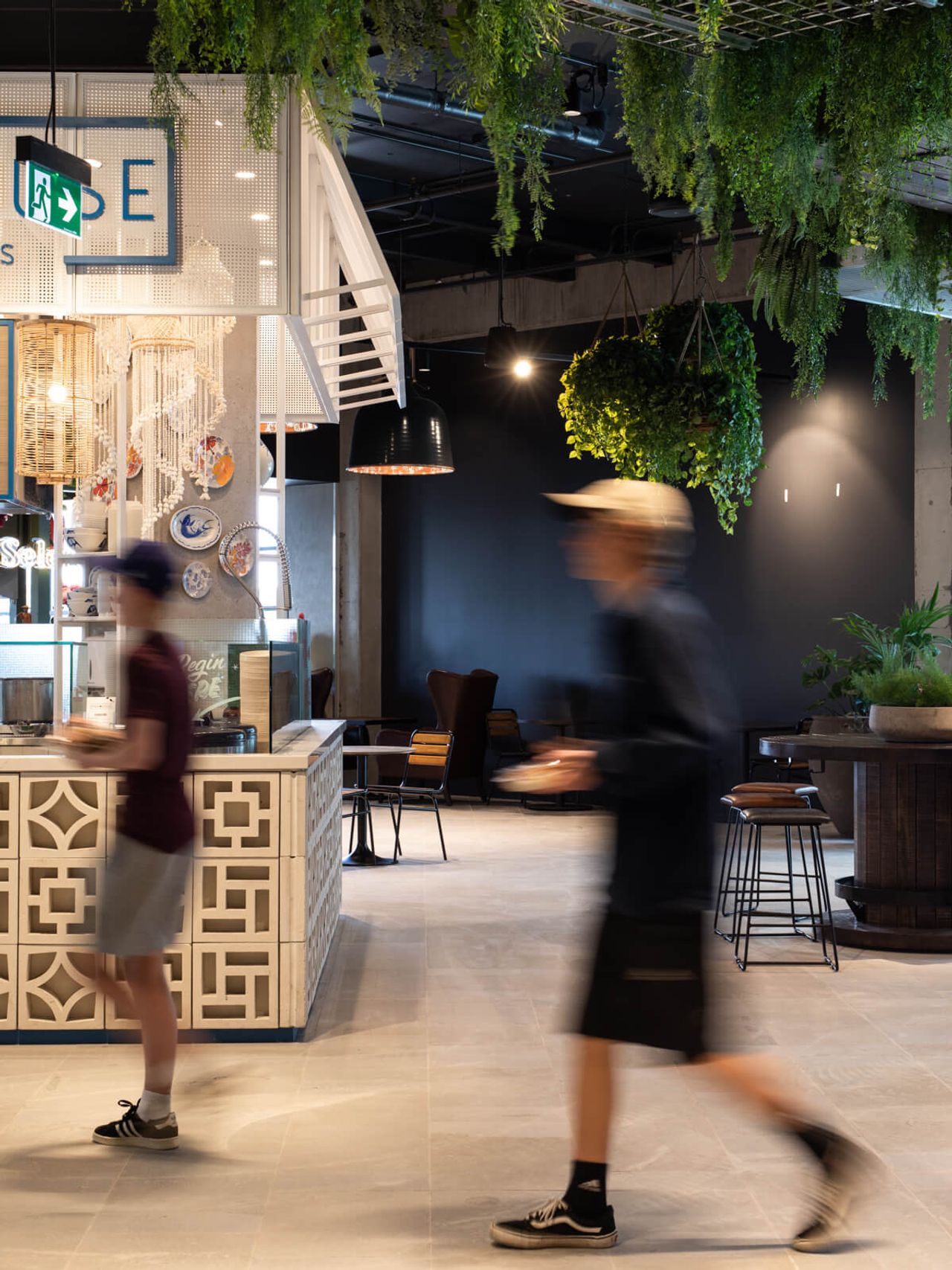 Blurred motion of customers walking past Poke House restaurant in Westfield Mall, highlighting patterned counters, hanging greenery, and stylish seating in a modern hospitality design space in Auckland.
