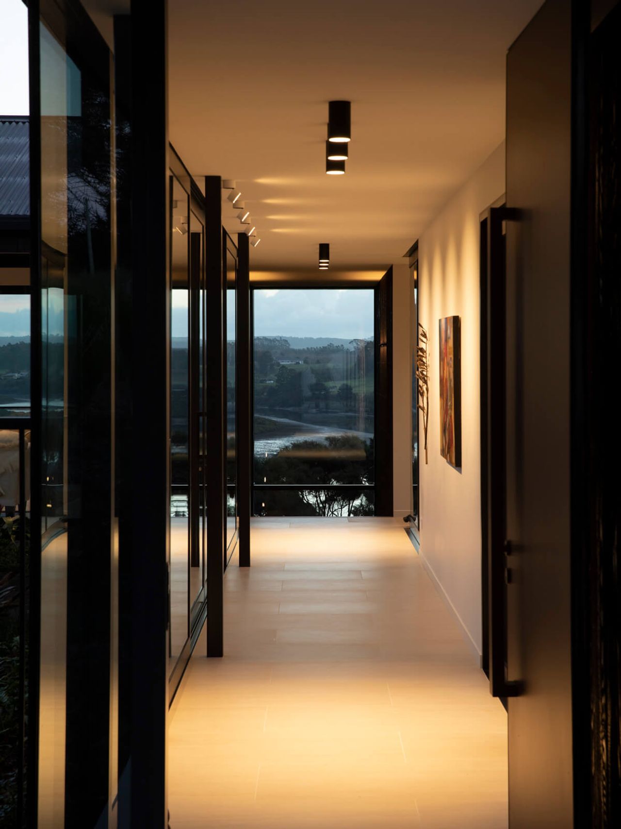Stylish interior hallway with modern lighting, glass walls, and a scenic view of the New Zealand countryside and water, highlighting contemporary architectural design.