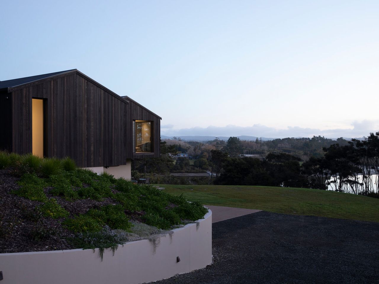 Modern architectural home with dark wood cladding overlooking a serene natural landscape and river view at sunset, showcasing sustainable home design and contemporary architecture in New Zealand.
